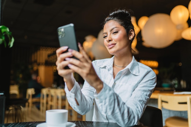 Hermosa chica latina usando su teléfono móvil en el café