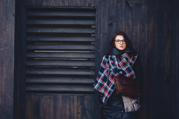 Hermosa chica en lentes y una bufanda contra una pared de madera