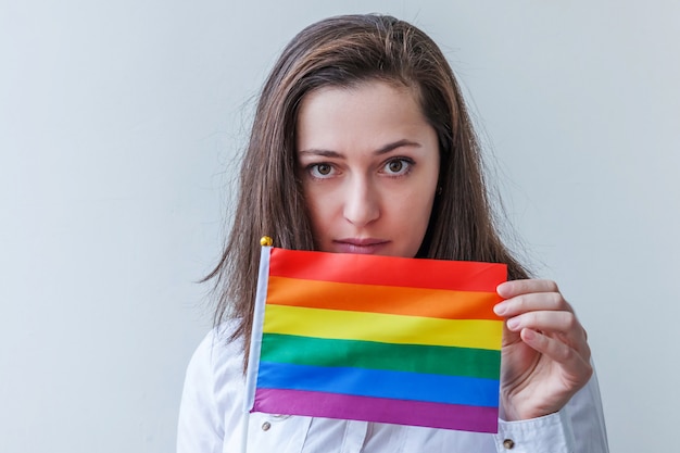 Hermosa chica lesbiana caucásica con bandera del arco iris LGBT aislada en la pared blanca mirando feliz y emocionada. Retrato de joven orgullo gay. Igualdad de derechos para el concepto de comunidad lgbtq.