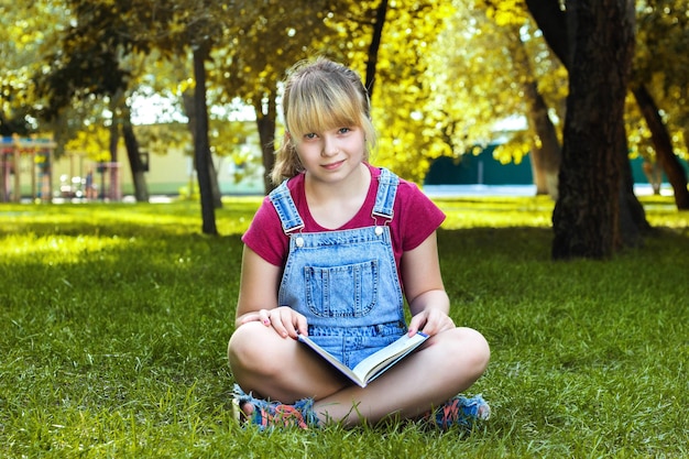 Hermosa chica leyendo un libro sentado en el césped en el parque