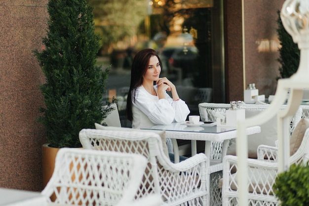 Una hermosa chica linda en un café bebe café en una mesa.