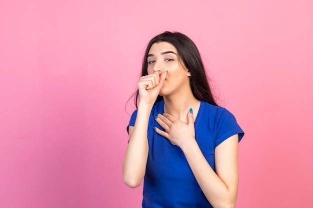 Foto hermosa chica llevándose la mano a la boca y de pie sobre fondo rosa foto de alta calidad