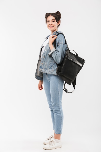 Hermosa chica de longitud completa con peinado de bollos dobles con ropa de jeans y mochila sonriendo, aislado en blanco