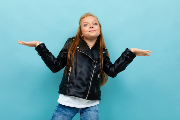 Hermosa chica en un look casual con una chaqueta de cuero y jeans extendió sus brazos a los lados en azul claro