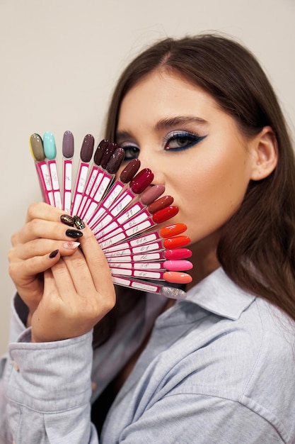 Hermosa chica con maquillaje azul cubre su rostro con una paleta con uñas para manicura