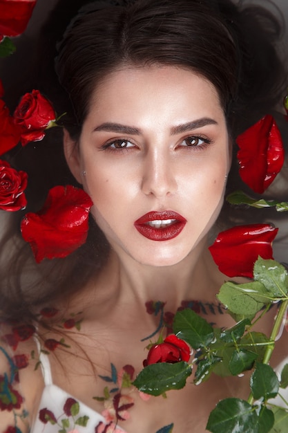 Hermosa chica con maquillaje clásico y labios rojos en el baño con flores. Rostro de belleza. Foto tomada en el estudio.