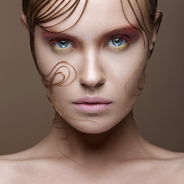 Hermosa chica con maquillaje de colores brillantes y mechones de cabello mojados en la cara.