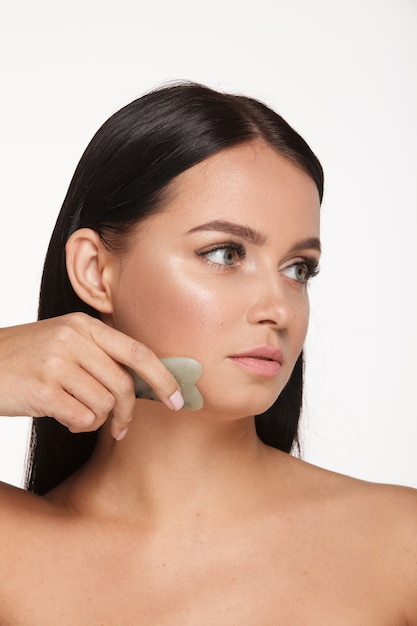 Foto hermosa chica con maquillaje natural y piel limpia sostiene en la mano un depurador facial de jade para adelgazar las arrugas anti envejecimiento