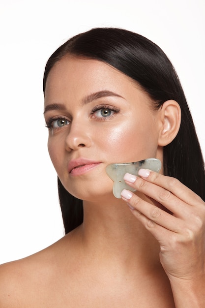 Hermosa chica con maquillaje natural y piel limpia sostiene en la mano un depurador facial de jade