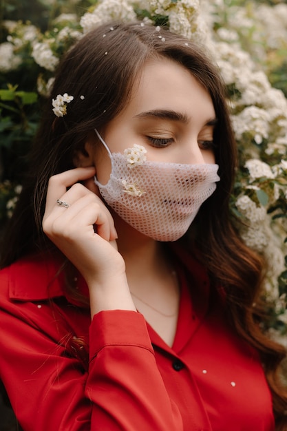 Hermosa chica en una máscara médica en arbustos en flor