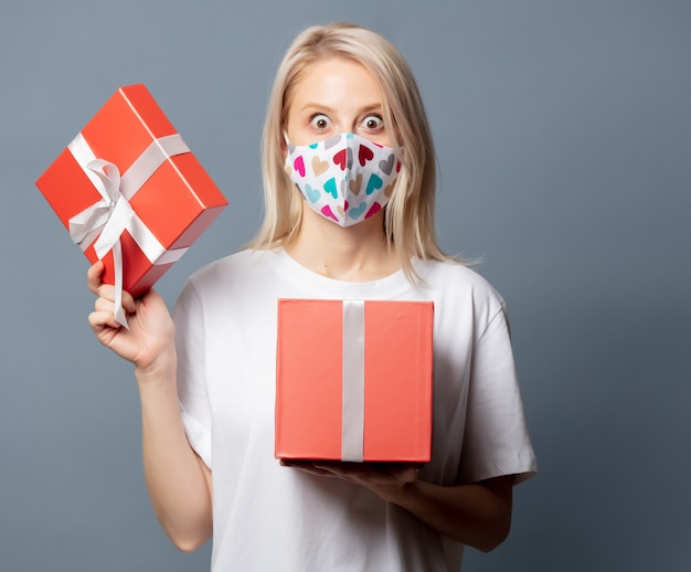 Hermosa chica en mascarilla con caja de regalo en espacio gris