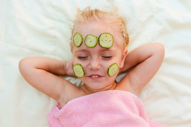 Hermosa chica con mascarilla facial de pepino.