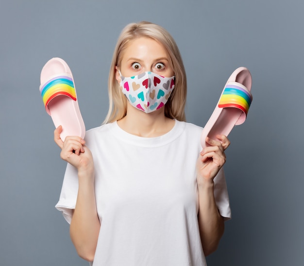 Hermosa chica en mascarilla con sandalias en espacio gris