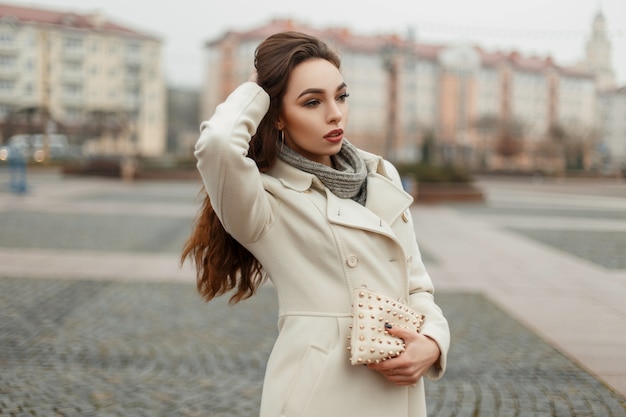 Hermosa chica de moda en un abrigo de moda con un elegante bolso en el día de otoño en la ciudad