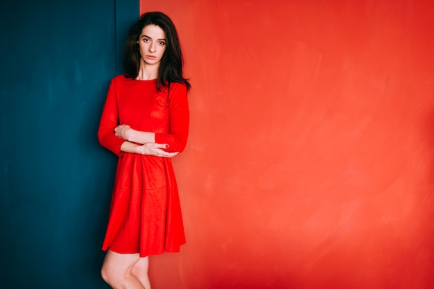 Foto hermosa chica de moda con cabello largo oscuro, apariencia española y cara sensual en elegante vestido rojo posando en la pared azul rojo.