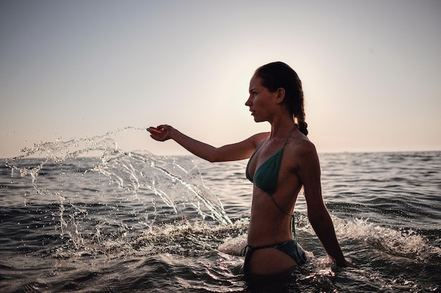 Hermosa chica modelo haciendo chapoteo en el mar al atardecer