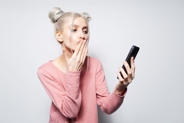 Hermosa chica con moños para el cabello enviando besos tomando selfie en el teléfono inteligente