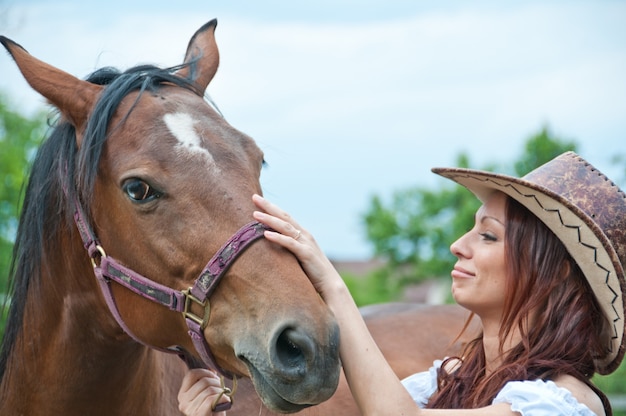 Hermosa chica morena acariciando un caballo