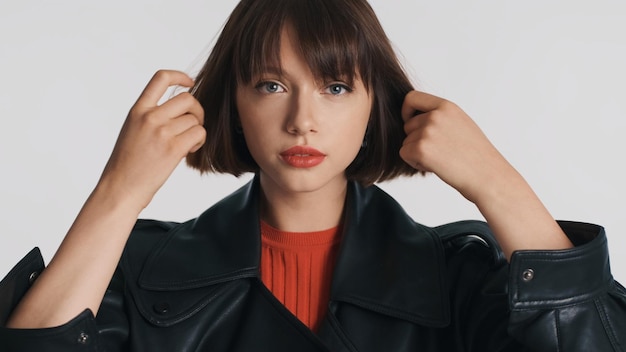 Hermosa chica morena con estilo con labios rojos acicalándose el pelo en la cámara aislada en el fondo blanco