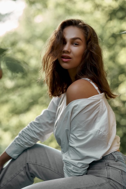 Hermosa chica morena en jeans y una camisa blanca posando sobre las ruinas del bosque