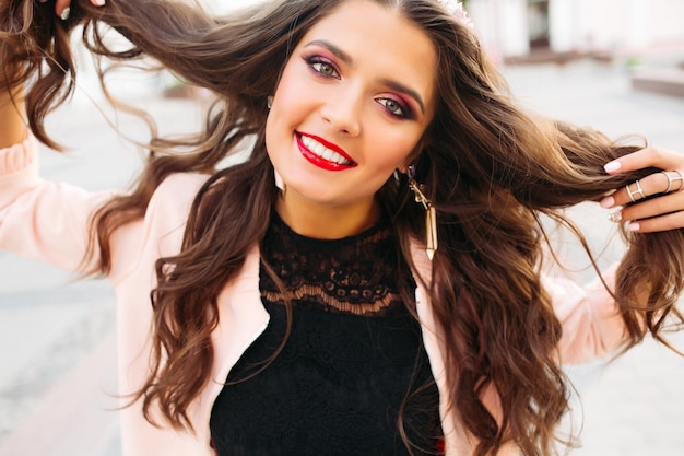 Hermosa chica morena con maquillaje brillante sosteniendo su cabello y sonriendo a la cámara.