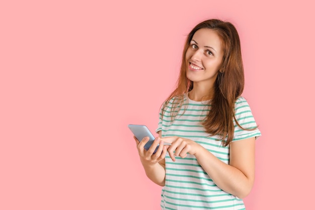 Una hermosa chica morena marca un número de teléfono en un teléfono inteligente. Retrato de una mujer sobre un fondo rosa con un teléfono móvil.