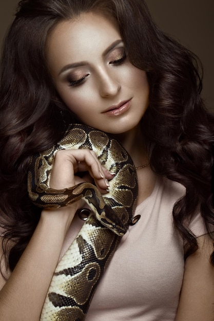 Hermosa chica morena modelo rizos perfectos y maquillaje de moda de noche con una serpiente en sus manos Cara de belleza