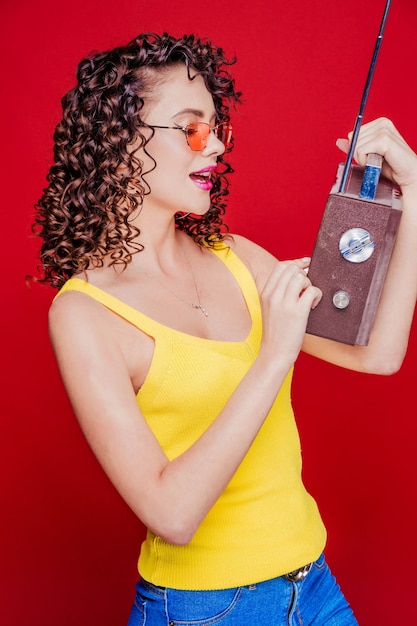 Hermosa chica morena con peinado rizado posando con una radio retro