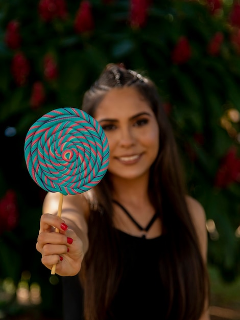 Hermosa chica morena con piruletas de colores en el bosque. Enfoque selectivo.