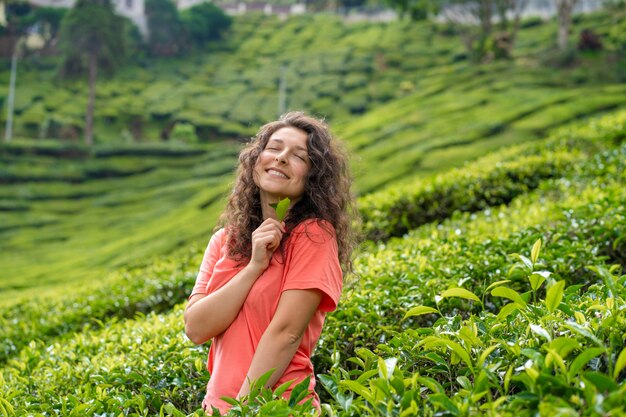 Hermosa chica morena posando en medio del valle del té entre arbustos de té verde.