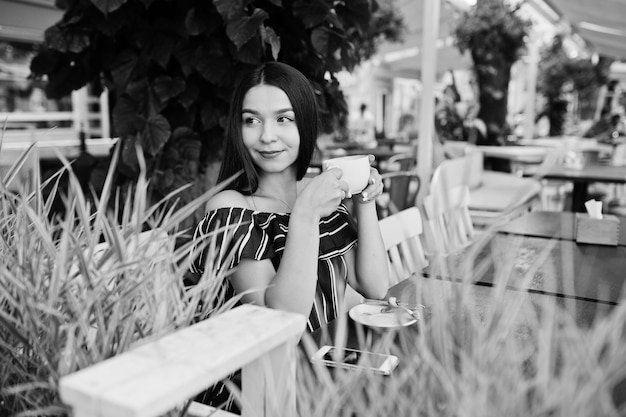 Hermosa chica morena sentada en la mesa de café con una taza de café y bebida