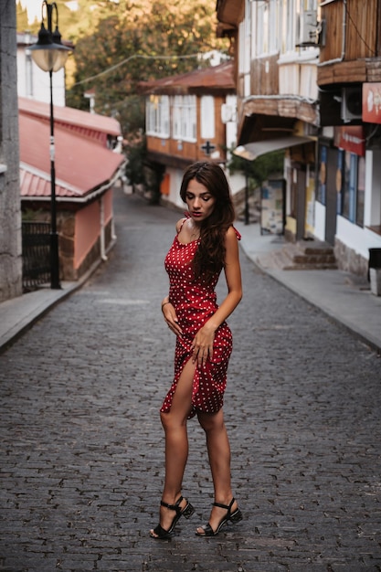 Hermosa chica morena sexy con un vestido rojo posando en la calle con adoquines en Italia
