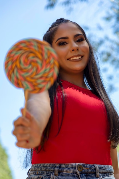 Hermosa chica morena sosteniendo piruleta de colores en el bosque Enfoque selectivo