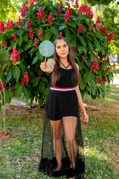 Hermosa chica morena sosteniendo piruleta de colores en el bosque Enfoque selectivo