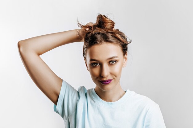 Una hermosa chica morena sostiene su cabello y hace su propio peinado. Modelo joven con pelo largo, maquillaje de moda con labios morados sobre un fondo gris. La mujer sonríe y mira a la cámara.