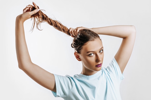 Una hermosa chica morena sostiene su cabello y hace su propio peinado