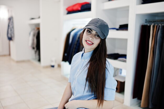 Hermosa chica morena en la tienda de ropa boutique en ropa casual y gorra.