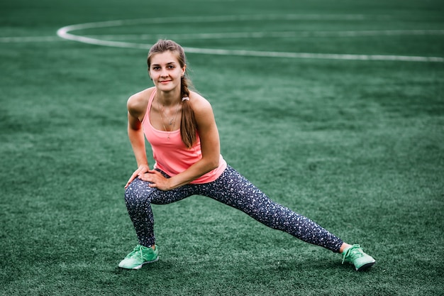 Una hermosa chica musculosa en medias y un chaleco hace un calentamiento en el estadio.