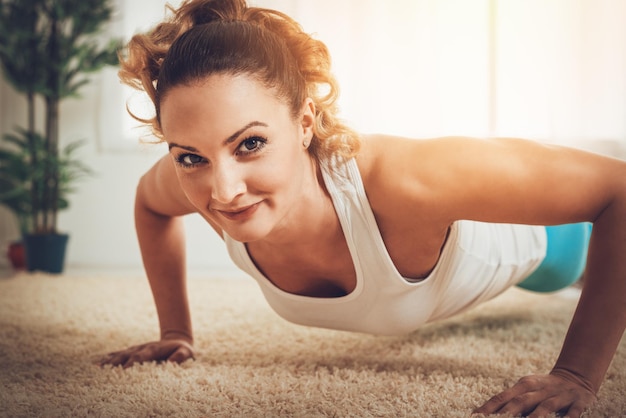 Hermosa chica musculosa sonriente haciendo flexiones en el piso. Mirando a la cámara.