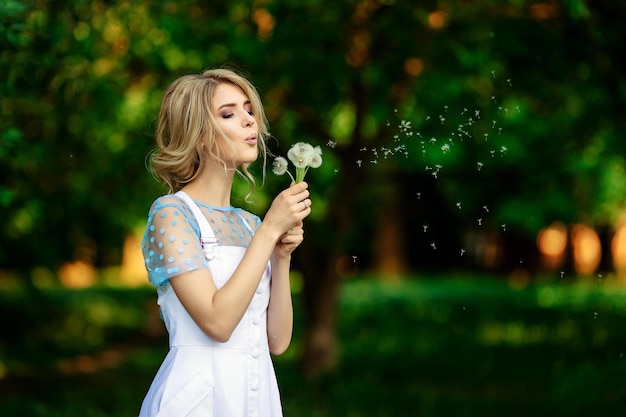 Hermosa chica en la naturaleza que sopla sobre un diente de león