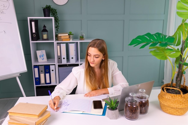 Hermosa chica de negocios mirando su computadora portátil mientras está de pie en la sala de oficina moderna. Concepto de negocio exitoso.