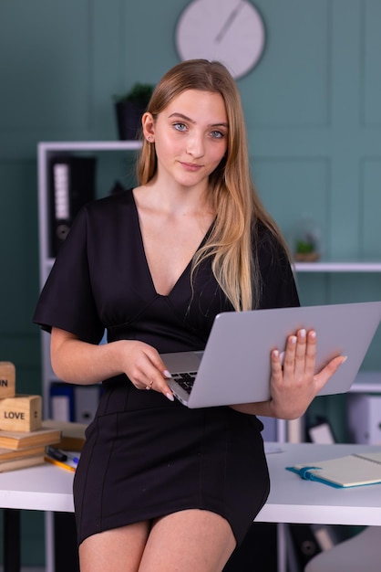 Hermosa chica de negocios mirando su computadora portátil mientras está de pie en la sala de oficina moderna.