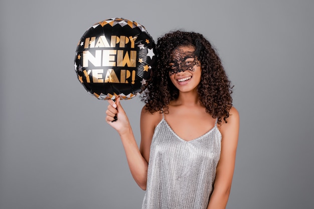 Hermosa chica negra con feliz año nuevo globo con máscara de mascarada aislada sobre gris