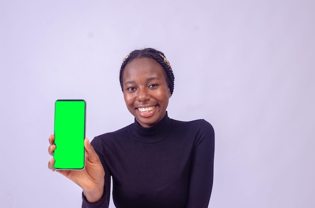 Hermosa chica negra muestra la pantalla de su teléfono mientras se siente feliz y emocionada con el concepto publicitario enfocado en su cara