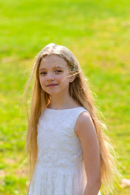 Hermosa chica de ojos azules con cabello largo y rubio con un vestido blanco caminando en el jardín de flores. Verano y primavera brillante, emotiva foto.