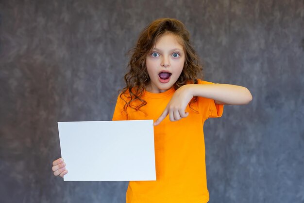 Una hermosa chica de ojos azules con una camiseta amarilla sosteniendo un pedazo de papel blanco se sorprende.