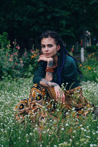 Hermosa chica de ojos marrones de cabello oscuro con una colorida falda étnica sentada entre las flores