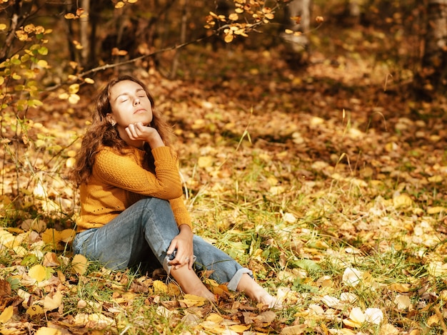 Hermosa chica en otoño Parque sentado sobre hojas caídas