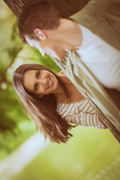 Hermosa chica en el parque con su novio disfruta jugando a esconderse detrás de un árbol.