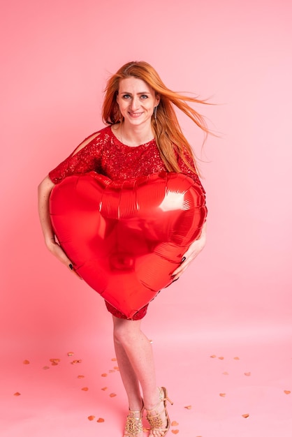 Hermosa chica pelirroja con globo de corazón rojo posando. Concepto de feliz día de San Valentín